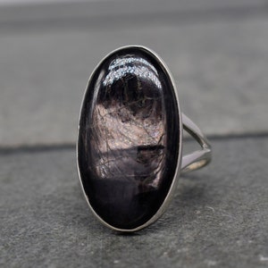 May include: A silver ring with a large oval-shaped black gemstone. The gemstone has a shimmering, iridescent effect.