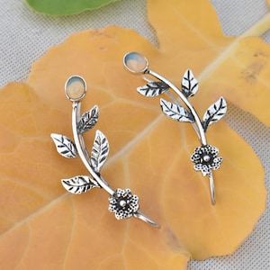 May include: A pair of silver ear cuffs with a delicate floral design. Each cuff features a small, white opal stone and a cluster of leaves.