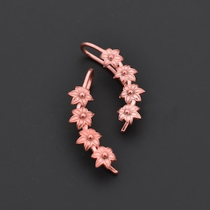 Pode incluir: Um par de brincos trepadores florais em ouro rosa. Cada trepador apresenta uma s&eacute;rie de flores detalhadas. Os brincos s&atilde;o projetados para curvar-se na orelha, oferecendo um estilo &uacute;nico e elegante. O fundo &eacute; cinza escuro s&oacute;lido.
