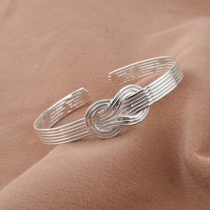 May include: A silver knot bracelet with a woven design. The bracelet is open and has a simple, elegant style.