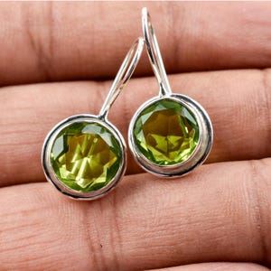May include: A pair of silver dangle earrings with round green peridot gemstones.