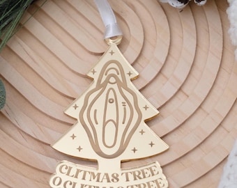 May include: A gold-colored Christmas tree ornament with the words "Clitmas Tree O Clitmas Tree". The ornament is shaped like a Christmas tree with a stylized vulva design. The ornament hangs from a white ribbon.