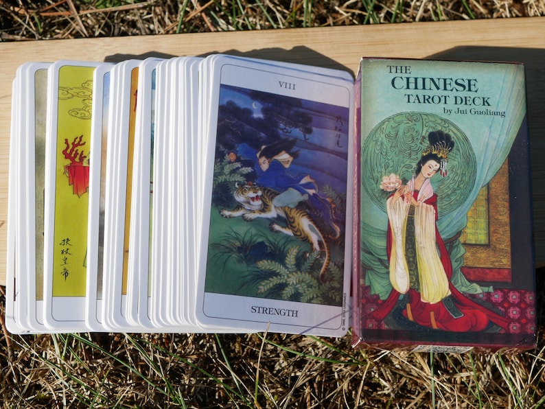 May include: A deck of tarot cards with a box. The cards feature colorful illustrations of Chinese art. The box reads "THE CHINESE TAROT DECK" by Jui Guoliang. The cards are fanned out, showing the "Strength" card with a tiger.