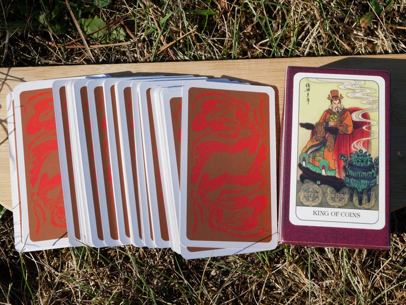 May include: A deck of tarot cards with a burgundy box. The card backs are brown with a red swirl design. The box shows a card with an illustration of a robed figure and the text "KING OF COINS".