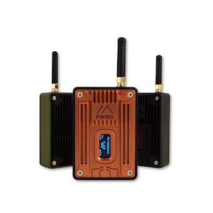 Op de afbeelding: Drie rechthoekige radiocommunicatieapparaten met verticale antennes. De centrale eenheid is koperkleurig met een klein digitaal scherm dat tekst weergeeft, terwijl de zij-eenheden olijfgroen en zwart zijn. Elk heeft een geribbelde metalen behuizing.