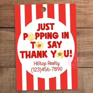 May include: A rectangular gift tag with a red and white vertical striped pattern. A central white circle features the red text JUST POPPING IN TO SAY THANK YOU! with popcorn illustrations, Hilltop Realty, and the phone number (123)456-7890.