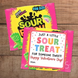 May include: Two packages of Sour Patch Kids candy with a Valentine's Day card. The candy packaging is pink and yellow with the words "SOUR THEN SWEET" and "FUN SIZE". The card reads "JUST A LITTLE SOUR TREAT FOR SOMEONE SWEET! Happy Valentine's Day!"
