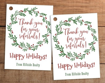 May include: Two white gift tags with a watercolour wreath design. The tags read "Thank you for your referrals!" and "Happy Holidays!" with the company name "From Hillside Realty" below. The tags have a hole at the top for stringing.