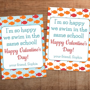 Puede incluir: Dos tarjetas del Día de San Valentín con un patrón de peces. Las tarjetas tienen el texto "¡Estoy tan feliz de que nadamos en la misma escuela! ¡Feliz Día de San Valentín! Tu amigo, Sophia".