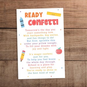 Puede incluir: Una tarjeta blanca con las palabras "READY CONFETTI" en rojo y naranja. La tarjeta tiene un poema sobre el comienzo de la escuela, con ilustraciones de un crayón, una regla, un lápiz y una manzana. El fondo es una superficie de madera.