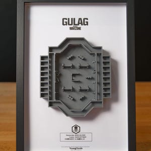 Puede incluir: Obra de arte enmarcada que presenta un modelo 3D gris del mapa Gulag Warzone. El texto "GULAG WARZONE" está en la parte superior, con información de lanzamiento en la parte inferior. El marco es negro.