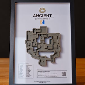 Pode incluir: Mapa 3D emoldurado do n&iacute;vel "Ancient" de Counter-Strike 2. O mapa cinza est&aacute; sobre um fundo branco com o logotipo e o texto do jogo. A moldura preta est&aacute; sobre uma superf&iacute;cie de madeira.