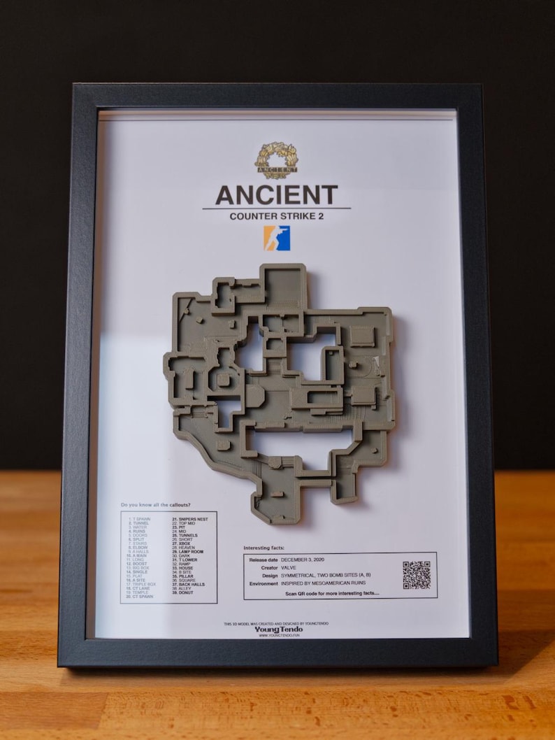 Pode incluir: Mapa 3D emoldurado do n&iacute;vel "Ancient" de Counter-Strike 2. O mapa cinza est&aacute; sobre um fundo branco com o logotipo e o texto do jogo. A moldura preta est&aacute; sobre uma superf&iacute;cie de madeira.