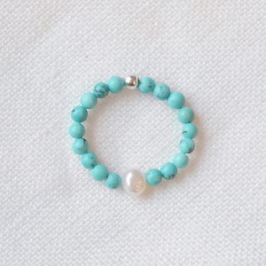 May include: A turquoise beaded ring with a single white pearl accent.