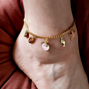 Puede incluir: Tobillera dorada con colgantes de concha, estrella de mar y pez. El colgante de concha tiene un acento de perla.