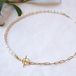 May include: A delicate gold chain necklace with a toggle clasp. Half of the necklace is made of small white pearls.