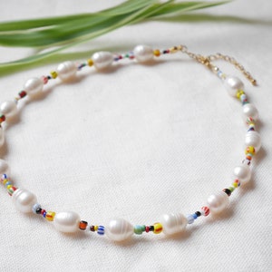 May include: A white pearl necklace with colourful beads. The necklace is made of oval-shaped pearls and small, colourful beads.