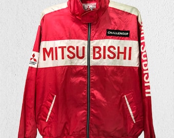 Op de afbeelding: Een rode windjack met witte accenten en de woorden "MITSUBISHI" en "CHALLENGER" erop gedrukt.