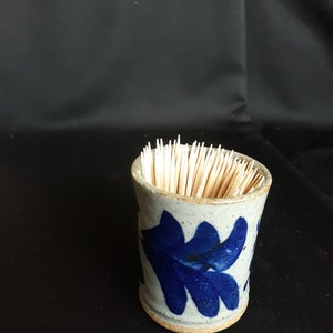 May include: A ceramic toothpick holder with a blue floral design. The holder is filled with toothpicks.