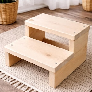 May include: A two-step wooden stool with a natural finish. The stool is rectangular, with a lower step and an upper step. The steps are connected by side supports. The stool is placed on a patterned rug.