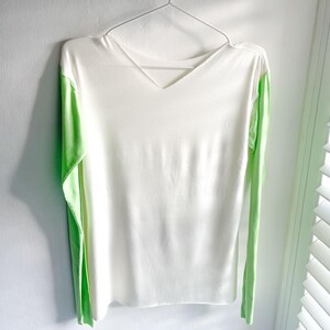 May include: White long-sleeved shirt with green trim on the sleeves. The shirt has a v-neck.