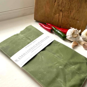 May include: An olive green waxed cotton potato sack with a linen bag liner. The sack has a white label with the text "WAXED COTTON POTATO SACK" and "PORTER ARBON". Red and green chillies, garlic, and a wooden chopping board are in the background.