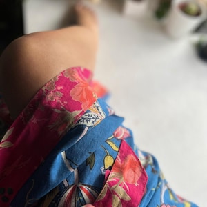 Puede incluir: Una bata de baño de estampado floral azul y rosa con ribete rosa. La bata está hecha de una tela suave y ligera.