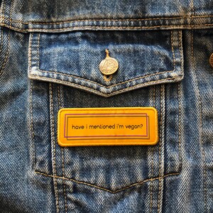 May include: A yellow and purple rectangular patch with the text "have i mentioned i'm vegan?" on a blue denim jacket.