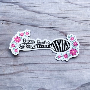 May include: A black and white zebra-striped spoon with pink flowers around it. The spoon has the text "Ehlers Danlos Warrior" on it.