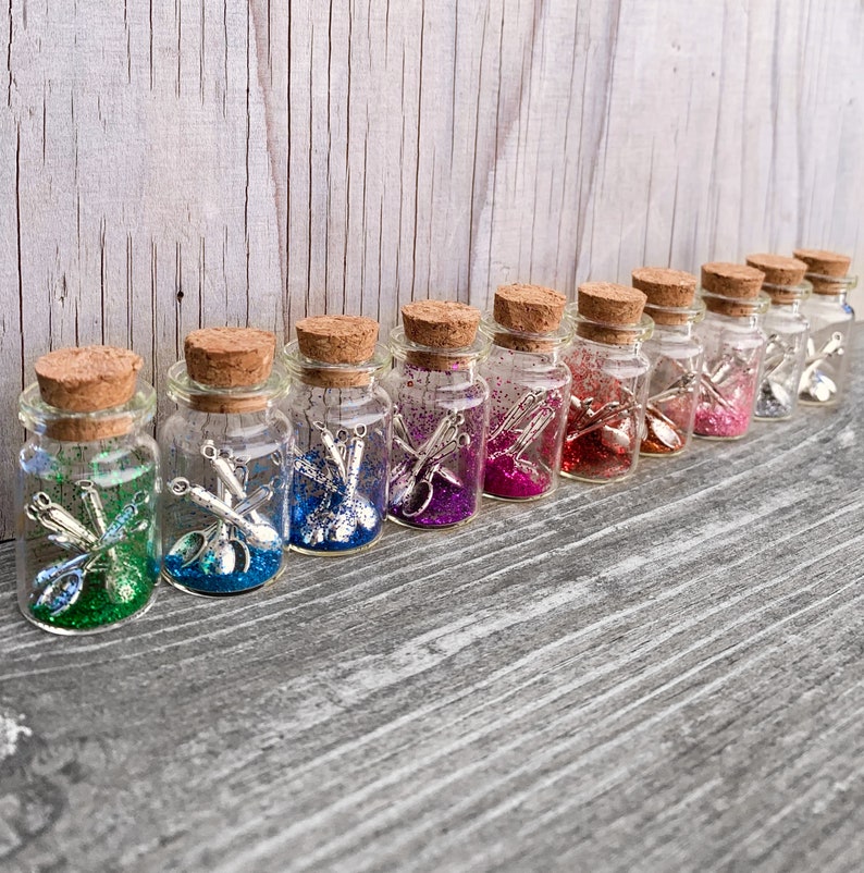May include: A row of ten small glass jars with cork lids filled with colourful glitter and miniature silver utensils.