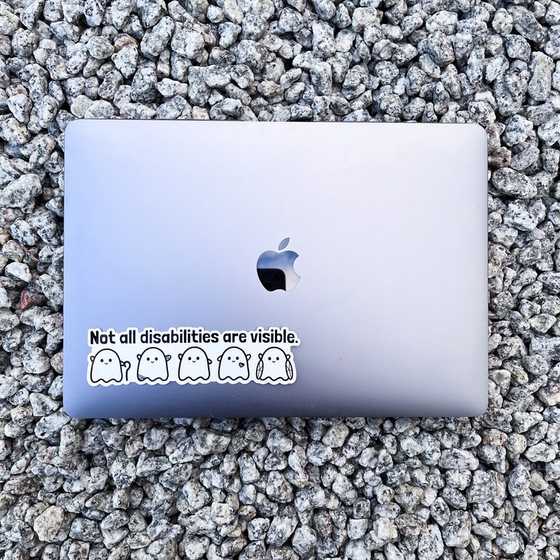 May include: A silver laptop with a sticker that reads "Not all disabilities are visible." The sticker features a line of five cartoon ghosts.