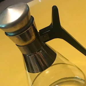 May include: A clear glass decanter with a gold rim and a black plastic handle. The decanter has a gold band around the middle.