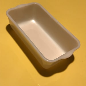 May include: A white ceramic loaf pan with a slightly rounded rectangular shape. The pan has a smooth, glossy finish.