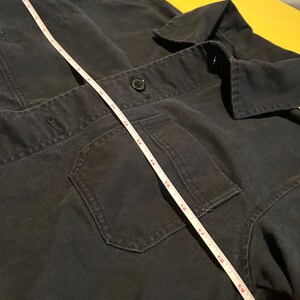 May include: Dark navy blue work jacket with a hood, two front pockets, and a button closure. A white measuring tape is laid across the jacket, showing a measurement of approximately 20 inches.