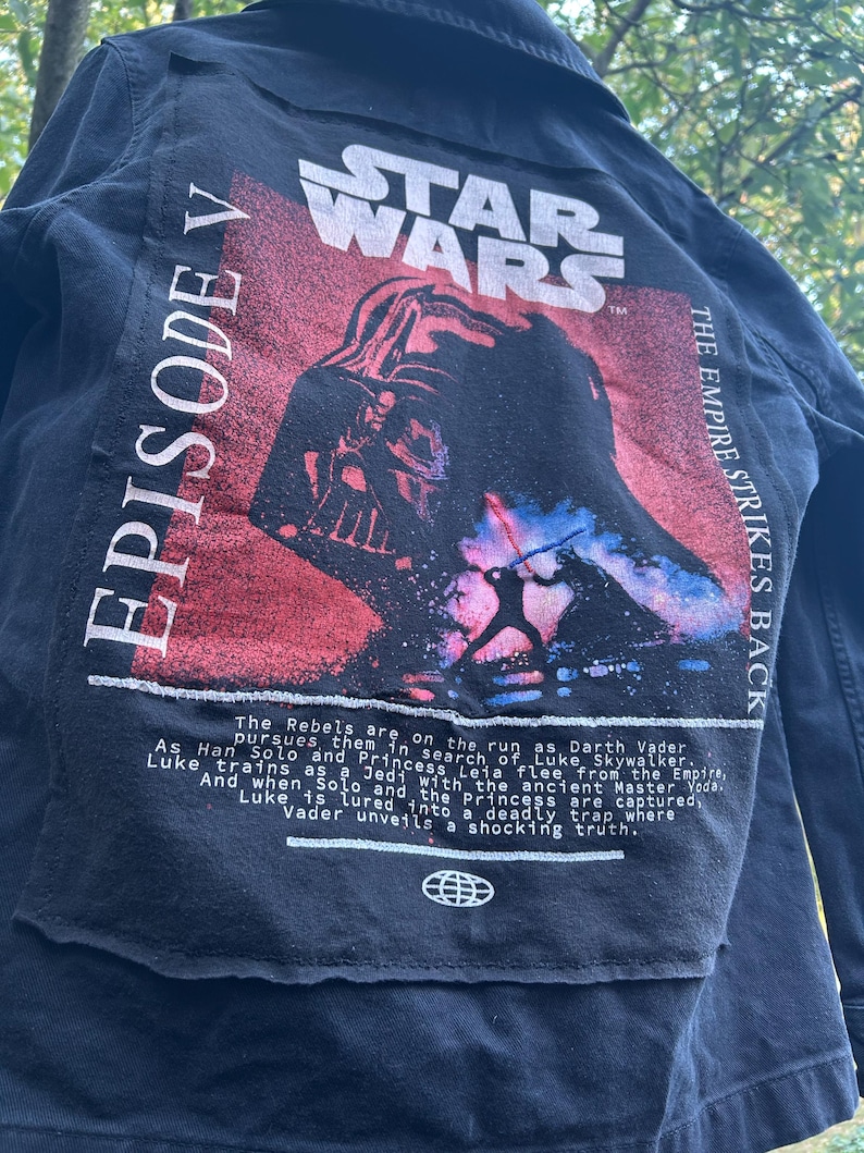 May include: Black denim jacket featuring a Star Wars graphic on the back. The design includes the Star Wars logo, Darth Vader, and text that reads "Episode V" and "The Empire Strikes Back."