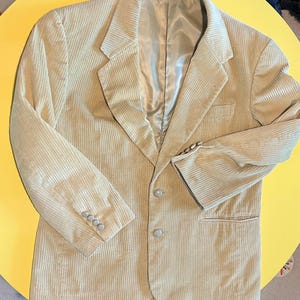 May include: Tan corduroy blazer with a notched lapel, three-button closure, and three buttons on each cuff. The blazer has a chest pocket and two lower pockets. The lining is a light satin material. The brand name "Clannl" is visible on the label.