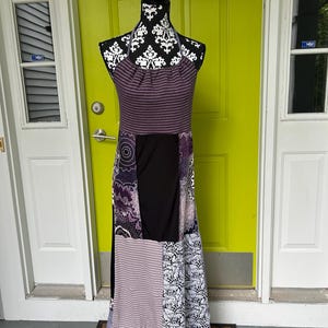May include: A patchwork maxi dress displayed on a mannequin. The dress features a halter neckline and a mix of patterns, including stripes, floral prints, and solid black panels. The color palette includes shades of purple, black, and white.