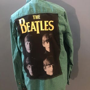 Puede incluir: Camisa de botones a cuadros verdes y blancos con un parche negro que presenta una foto de The Beatles y el texto "THE BEATLES" en letras doradas.