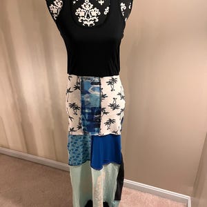 May include: A black tank top paired with a patchwork maxi skirt. The skirt features panels of white fabric with black palm trees, blue patterns, and solid blue and teal sections. The dress is displayed on a mannequin.