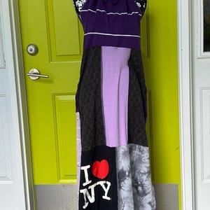 May include: A patchwork maxi dress on a mannequin. The dress features a purple halter top, a lavender panel, and a black panel with "I NY" text. The skirt has a mix of patterns and colors, including tie-dye and geometric prints.
