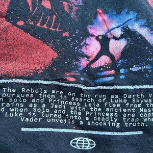 May include: Black t-shirt featuring a Star Wars graphic with Darth Vader and Luke Skywalker in a lightsaber duel. The text reads "The Rebels are on the run..." and includes a globe logo.