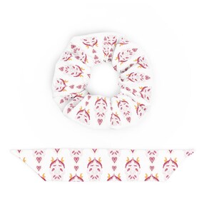 Puede incluir: Un scrunchie blanco con un patrón floral rosa y dorado. El scrunchie se muestra con una liga para el cabello a juego.