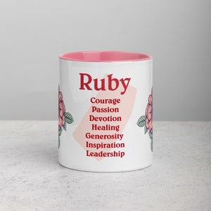 Puede incluir: Taza de cerámica blanca con borde rosa. La taza presenta el nombre "Ruby" en letras rojas y una lista de palabras en letras rojas debajo del nombre: Coraje, Pasión, Devoción, Sanación, Generosidad, Inspiración, Liderazgo. La taza está decorada con diseños florales rosas.