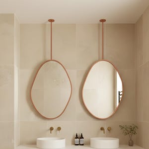 Puede incluir: Un baño moderno con una paleta de colores neutros. Dos espejos ovalados cuelgan sobre un mueble de lavabo doble. Un mueble de madera con líneas verticales ofrece almacenamiento. Un toallero negro y un inodoro blanco completan el espacio.