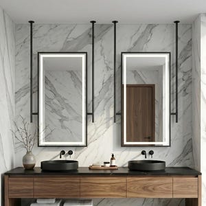 Puede incluir: Un mueble de baño con un armario largo de madera, dos lavabos circulares negros y dos espejos rectangulares suspendidos del techo por varillas de metal negro. La pared y el suelo están cubiertos de mármol blanco con vetas grises.