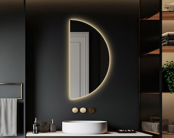 May include: A modern bathroom with black walls, white marble, and a wooden vanity with two drawers. A half-round mirror hangs above the sink, and a shelf unit with a potted plant sits on the right side of the image.