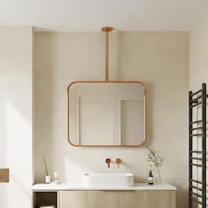 Pode incluir: Interior de casa de banho moderno com uma bancada de madeira clara e um espelho com moldura de cobre. A bancada tem duas gavetas e uma prateleira aberta. Um toalheiro preto está montado na parede. O espelho tem cerca de 60 cm de largura.