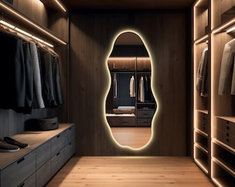 Op de afbeelding: Een moderne walk-in closet met houten panelen en warme verlichting. De kast heeft een grote, onregelmatig gevormde spiegel en meerdere planken en laden voor opslag.