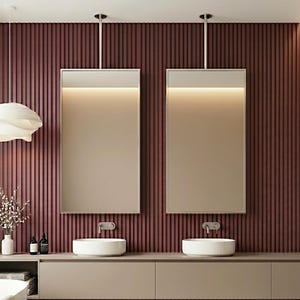 Könnte beinhalten: Ein Badezimmer-Waschtischbereich mit einer dunkelroten, vertikal geriffelten Wand, zwei von der Decke hängenden rechteckigen Spiegeln mit integrierter Beleuchtung, zwei weißen Aufsatzwaschbecken und einem langen, hellbeigen Hängeschrank.