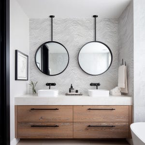 May include: A modern bathroom vanity with two round, black-framed mirrors suspended from the ceiling. The vanity features a light wood cabinet with four drawers, white countertops, and two white rectangular sinks. The background has a wavy, black and white patterned wallpaper.
